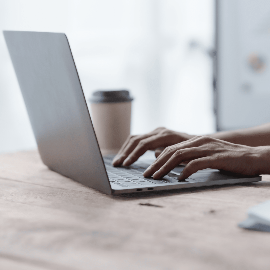 A person is seated in a cafe working on a laptop with a cup of coffee.