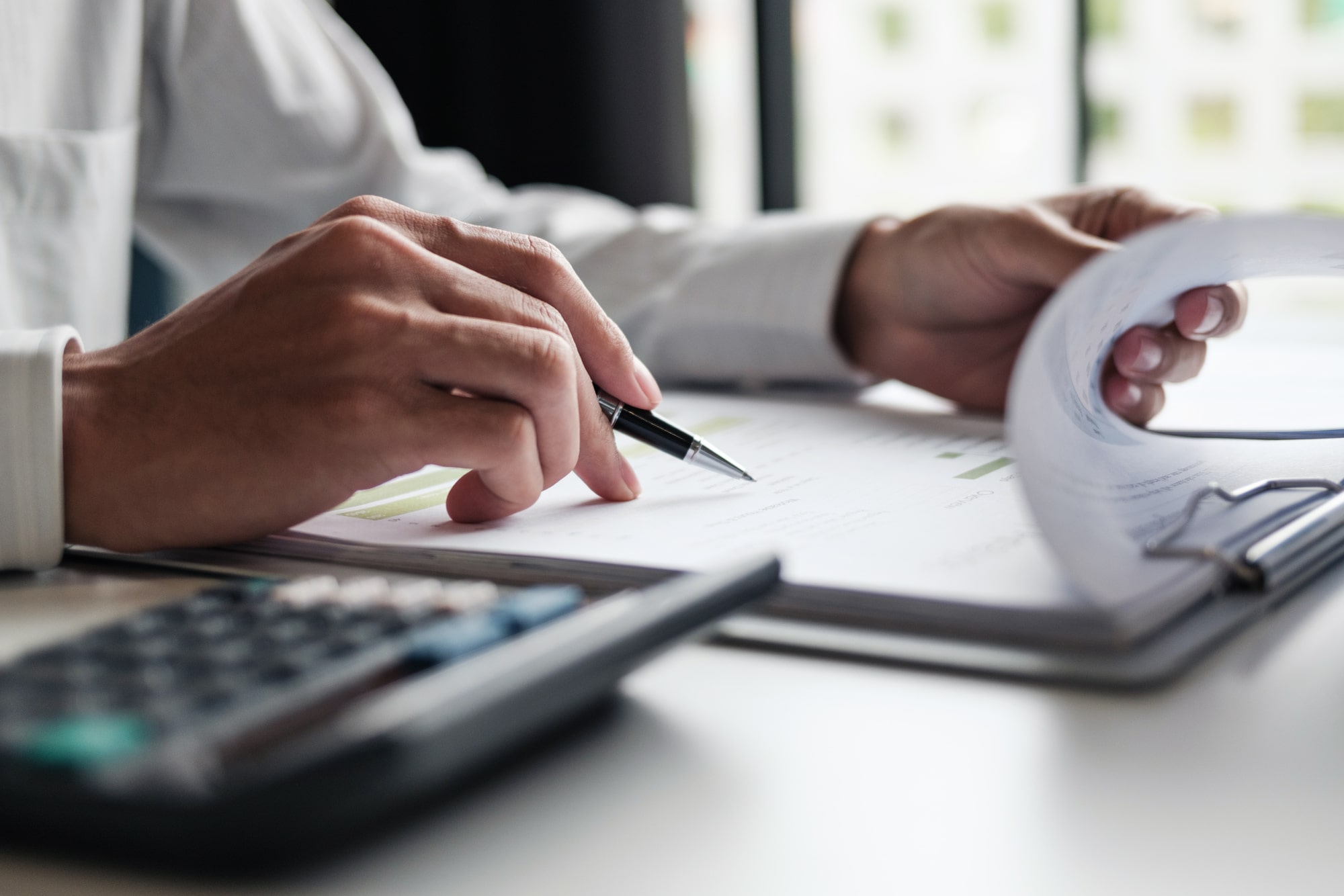 Man seated with pen and calculator, reviewing financial documents.